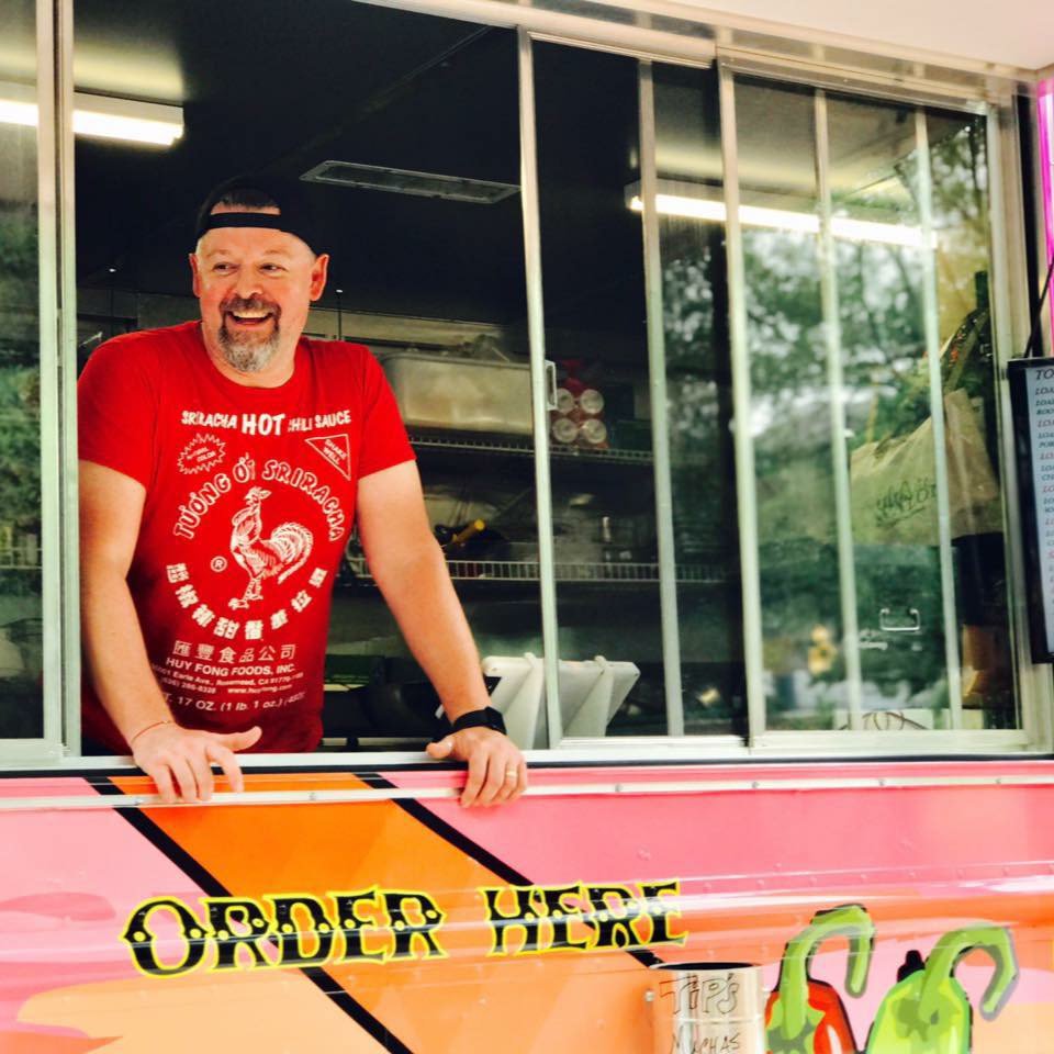 Man in red T-shirt and black baseball hap at window of pink food truck
