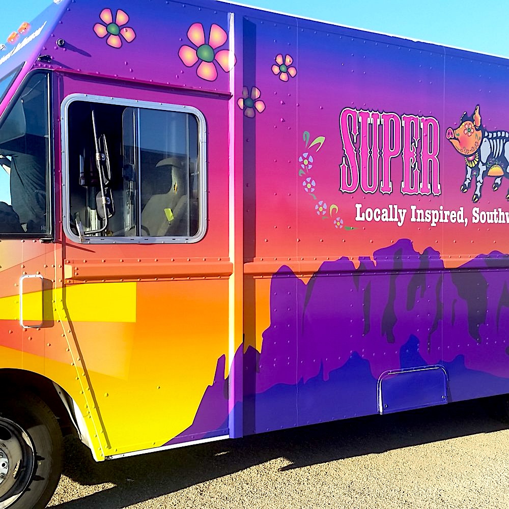 A yellow, purple, and pink food truck with mountains painted on the side
